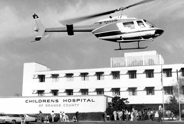 Helicopter flying above hospital building with people on the ground
